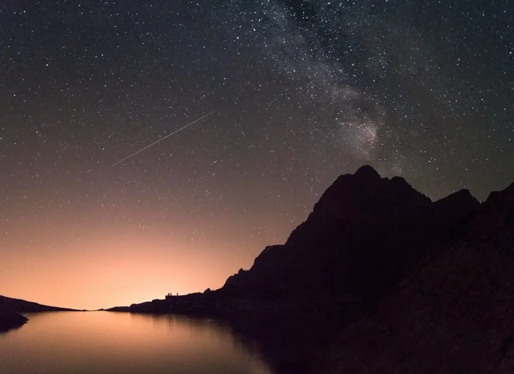 Ciel constellé d'étoiles dont la lumière se reflète sur un lac de montagne.