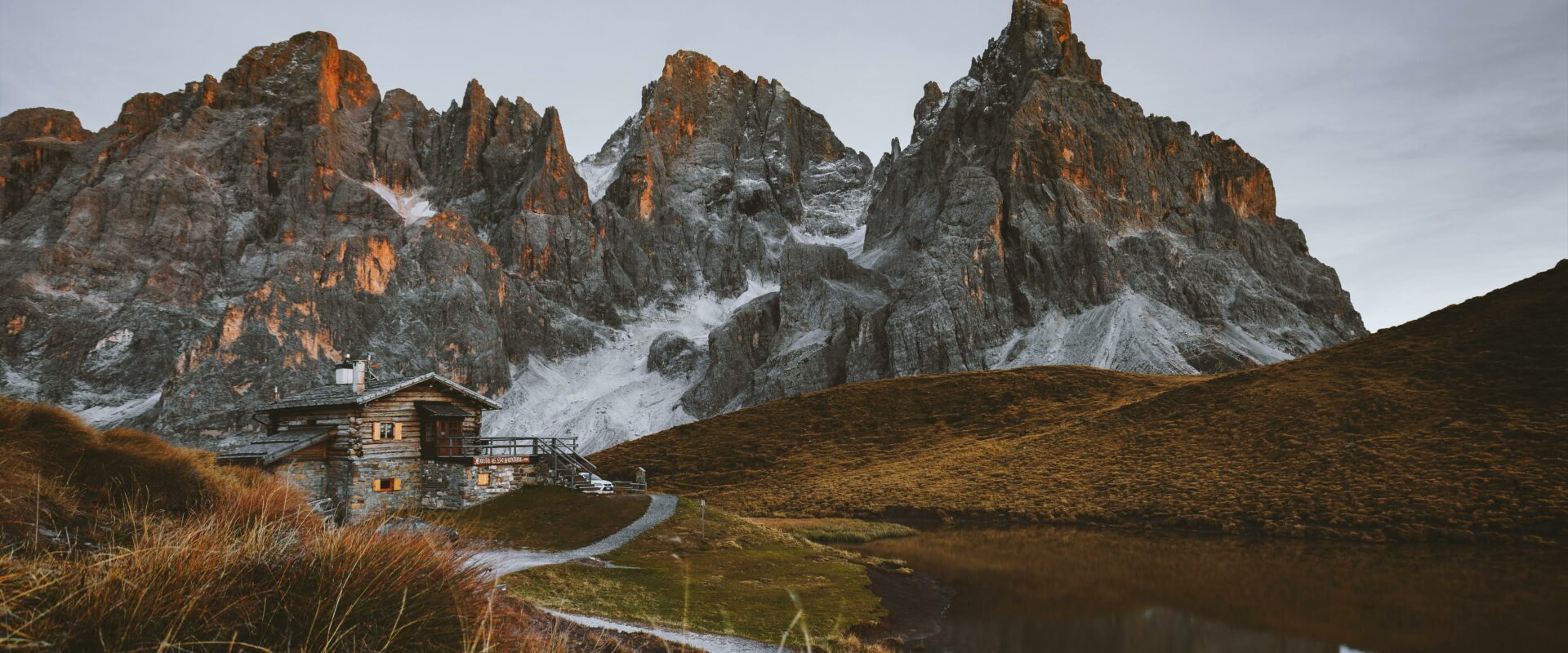 Refuge de montagne avec des couleurs automnales à côté d'un lac et à proximité de sommets très découpés.